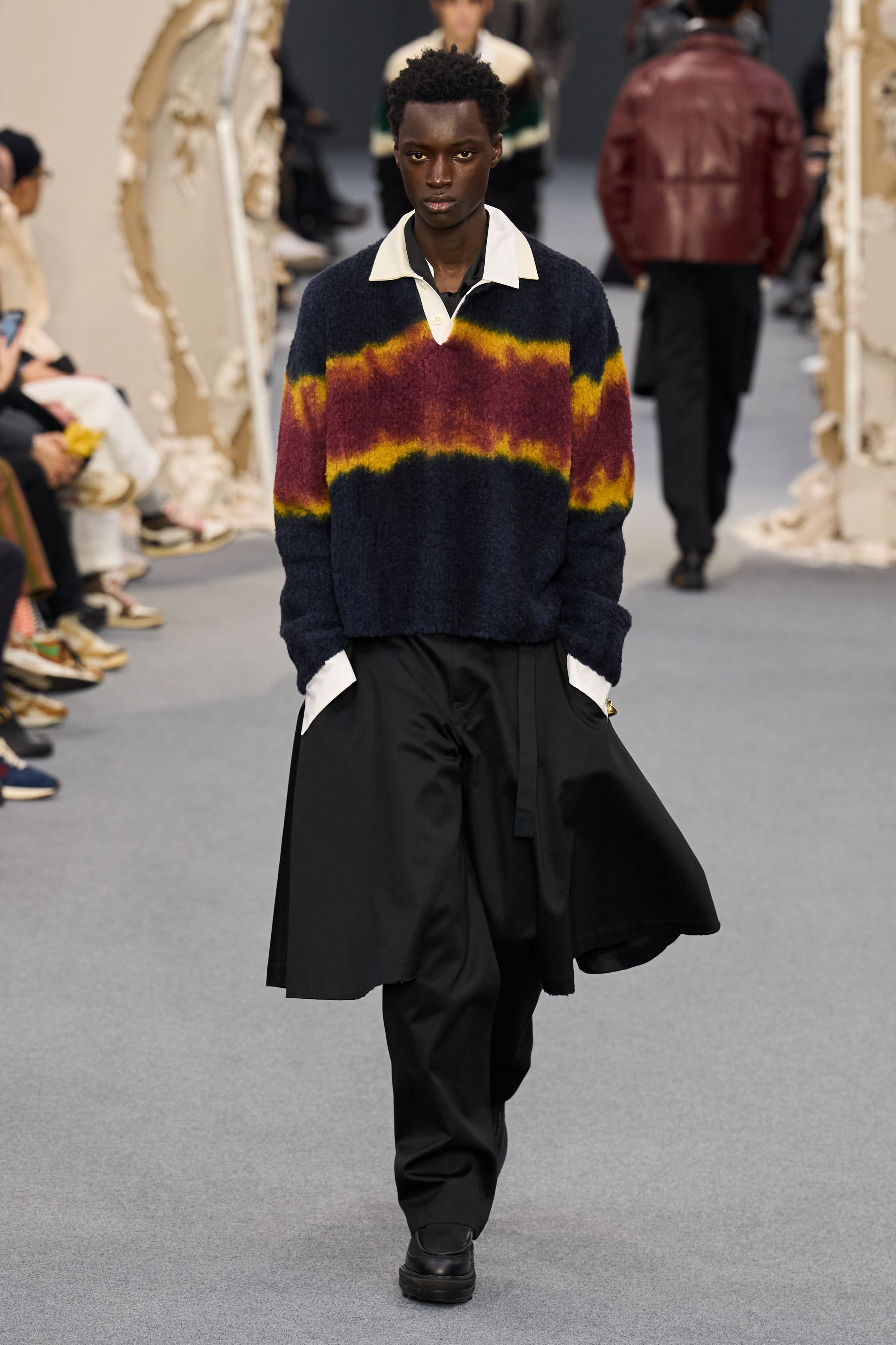 Sacai 2026秋冬再次展示其无可复制的“混合美学”。正装、牛仔、皮草与制服元素被高度结构化地拼接，形成既熟悉又陌生的服装形态。性别边界被进一步模糊，层叠结构制造流动节奏，使行走本身成为设计的一部分。系列在秩序与混乱之间找到平衡，是Sacai 对当代复杂生活状态的持续回应-顽石频道趋势研究